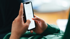 An anonymous teenage boy typing text messages on his smartphone while lying on a couch at home.
